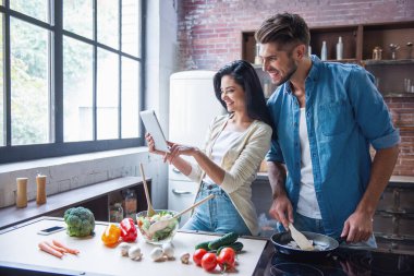Güzel genç çift dijital tablet kullanma ve evde mutfakta yemek yaparken gülümseyen