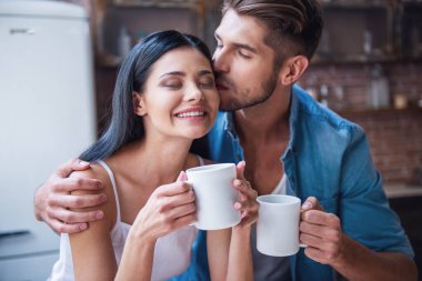 Güzel genç çift sarılma ve evde Mutfakta çay yudumlarken gülümseyerek. Adam çekici onun kız öpüyor