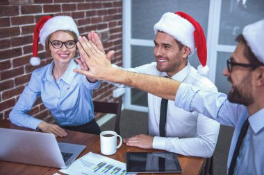 Mutlu Noel Baba şapkaları iş adamları yüksek beş veren ve süre kutlama yeni yıl Office gülümseyen