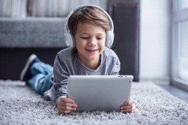 Küçük çocuk Kulaklığımda dijital tablet kullanma ve yerde evde yatarken gülümseyen