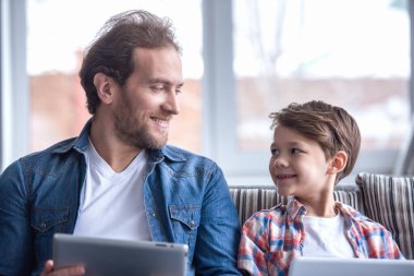 Baba ve oğul dijital tablet kullanma ve birlikte evde vakit ise gülümseyen