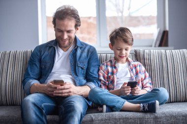 Baba ve oğul akıllı telefonlar kullanarak ve birlikte evde vakit ise gülümseyen