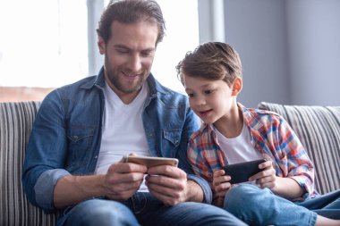 Baba ve oğul akıllı telefonlar kullanarak ve birlikte evde vakit ise gülümseyen
