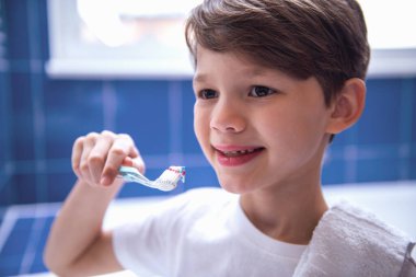 Küçük çocuk banyoda diş fırçalama sırasında gülümsüyor