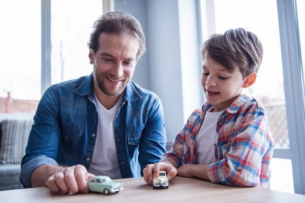 Father and son are playing with toy cars and smiling while spending time together at home