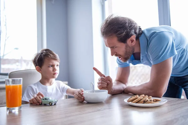 Father is edifying his son who is playing with toy car and refusing to eat