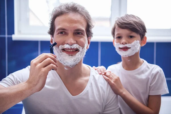 Father and son are smiling while shaving in bathroom