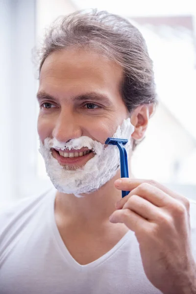 ハンサムな男はバスルームで剃毛しながら笑っています — ストック写真