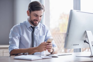 Yakışıklı işadamı bir smartphone kullanarak ve ofiste çalışırken gülümseyen