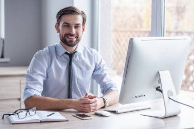 Yakışıklı işadamı kameraya bakarak ve bir bilgisayar Office ile çalışırken gülümseyen