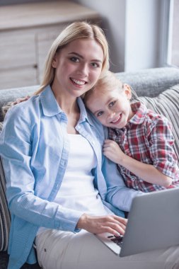 Güzel genç anne ve sevimli küçük kızı bir dizüstü bilgisayar kullanarak ve birlikte vakit ise gülümseyen