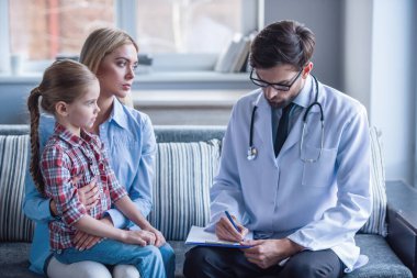 Güzel genç anne ve çocuk doktoru, küçük kızı. Doktor notlar yapıyor