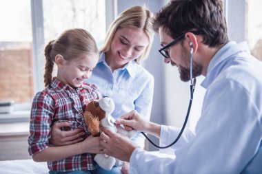 Güzel genç anne ve çocuk doktoru, küçük kızı. Doktor biraz sabırlı bir stetoskop kullanarak incelenmesi