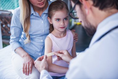 Güzel genç anne ve çocuk doktoru, küçük kızı. Doktor yapışkanlı bandaj kullanıyor