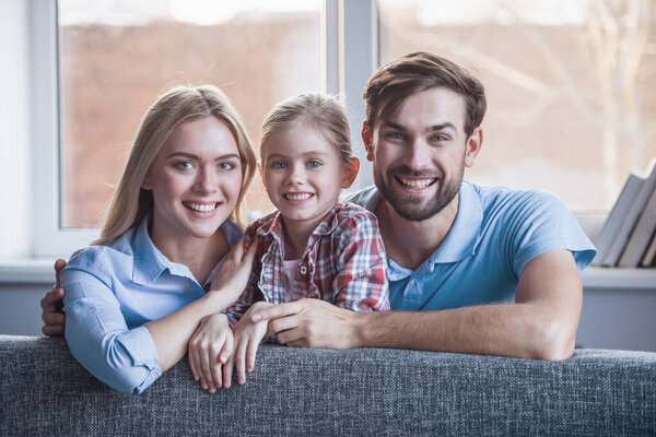 Portrait of beautiful young parents and their cute little daughter hugging, looking at camera and smiling