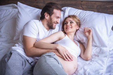 Güzel hamile kadın ve yakışıklı kocası sarılma ve yatakta birlikte vakit ise gülümseyen