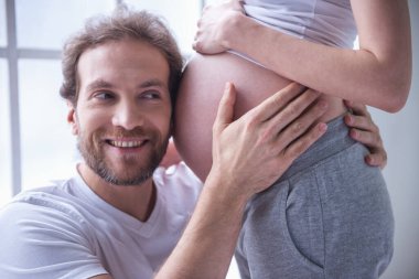 Yakışıklı adam güzel hamile karısının karnını dinliyor ve gülümsüyor.