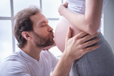 Yakışıklı adam, güzel hamile karısının karın öpüyor