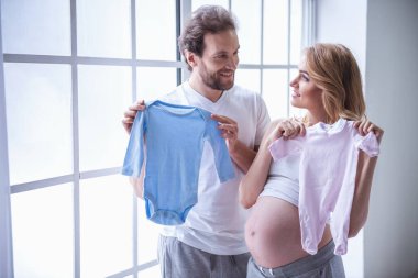 Güzel hamile kadın ve yakışıklı kocası bebek bodysuits tutarak ve gülümseyen