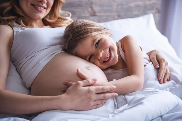 Menina Bonito Está Abraçando Barriga Sua Bela Mãe Grávida Sorrindo — Fotografia de Stock