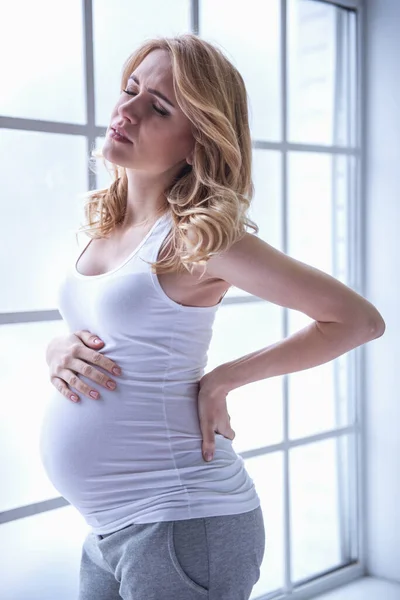 Beautiful tired pregnant woman is touching her tummy and keeping one hand on her back