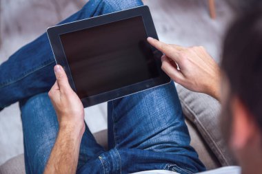 Yakışıklı adam kanepede otururken dijital tablet kullanma jean giysiler içinde Resim kırpılmış