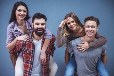 Güzel Genç çiftler kameraya bakıyor ve gülümsüyor, gri arka plan üzerinde. Kızlar pickaback oturuyorsun
