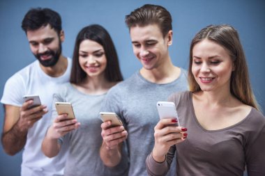 Güzel genç insanlar akıllı telefonlar kullanarak ve gri arka plan üzerinde gülümseyen