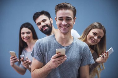 Güzel genç insanlar akıllı telefonlar kullanarak ve gri arka plan üzerinde gülümseyen