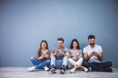 Güzel genç insanlar akıllı telefonlar kullanarak ve yerde otururken gülümseyen