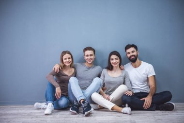 Güzel genç arkadaşlar sarılma, kameraya bakıyor ve gri arka plan üzerinde katta otururken gülümseyen