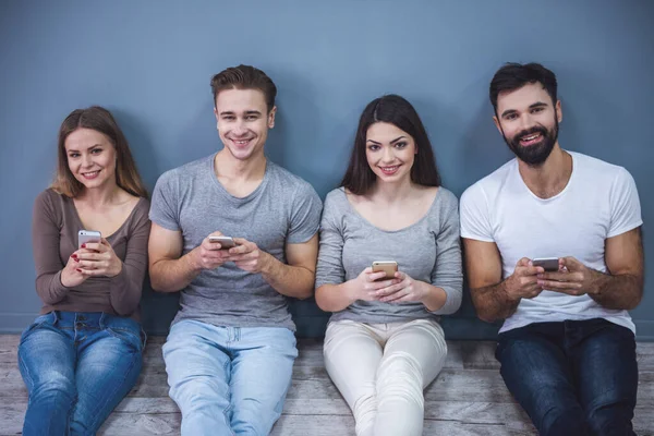 Güzel genç insanlar akıllı telefonlar kullanarak ve yerde otururken gülümseyen