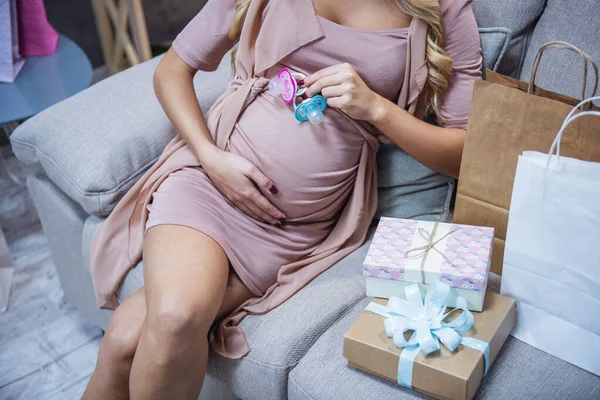 Bebek duş sırasında kanepede otururken yenidoğan emzikler tutan güzel hamile kadın Resim kırpılmış