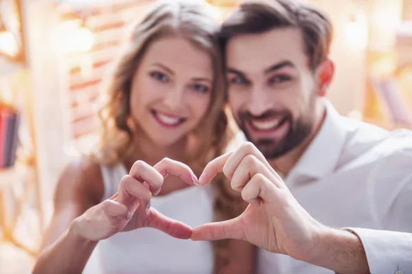 Beautiful young couple is making heart of fingers and smiling while celebrating at home