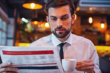 Yakışıklı işadamı bir gazete okuyor, kahve içme ve kafede otururken gülümseyen