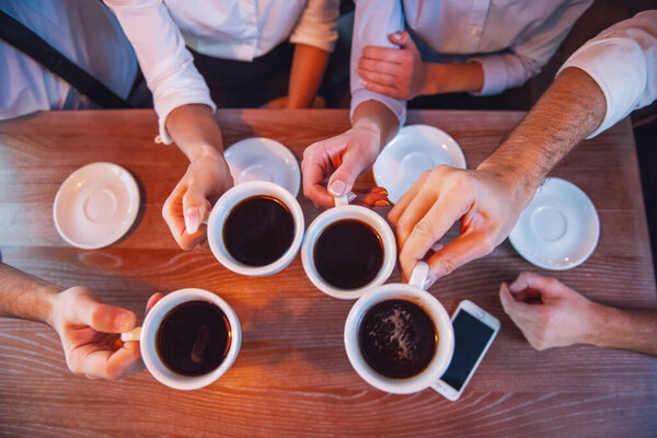 Top view of business people holding cups of coffee while having coffee break in cafe