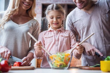 Sevimli küçük kız ve güzel ailesi sebze kesme ve evde mutfak salata yaparken gülümseyen