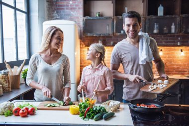 Sevimli küçük kız ve güzel ailesi evde yemek pişirirken gülümsüyorlar.