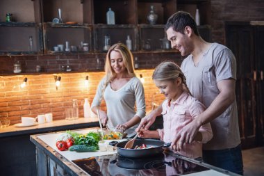 Sevimli küçük kız ve güzel ailesi evde yemek pişirirken gülümsüyorlar.