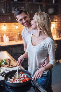 Güzel genç çift birlikte evde mutfakta yemek yaparken gülümsüyor