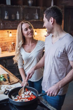 Güzel genç çift birbirine bakarak ve birlikte evde mutfakta yemek yaparken gülümseyen