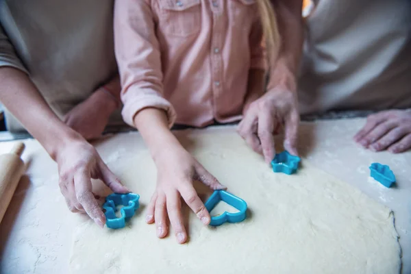 Cropped image of little girl and her parents using cookie cutters while baking in kitchen at home