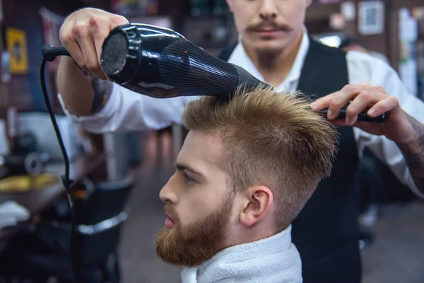 Handsome bearded man is getting hairstyle by hairdresser at the barbershop