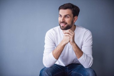 Yakışıklı genç adam uzakta seyir ve gri arka plan üzerinde gülümseyen