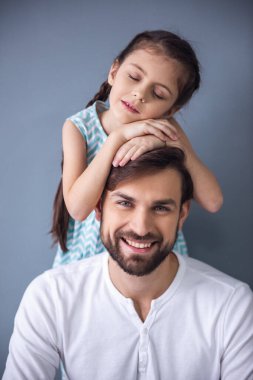 Sevimli küçük kız ve kameraya poz ve gri arka plan üzerinde gülümseyen yakışıklı babası portre