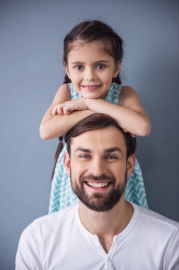Sevimli küçük kız ve kameraya bakarak ve gri arka plan üzerinde gülümseyen yakışıklı babası portre
