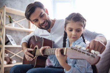 Sevimli küçük kız ve yakışıklı babası gitar çalmak ve evde kanepede otururken gülümseyen
