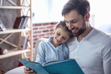 Sevimli küçük kız ve yakışıklı babası bir kitap okuma ve evde kanepede otururken gülümseyen