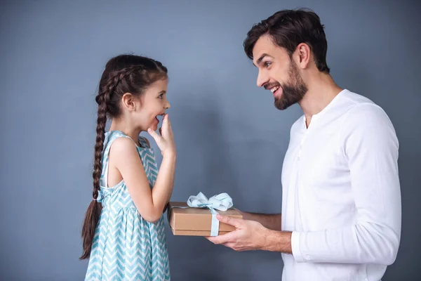 Handsome young father is giving a gift box to his cute little daughter. Both are smiling