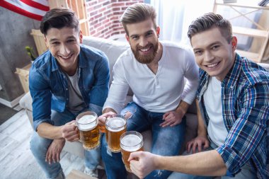 Çekici tungur bardak bira, kameraya bakarak ve evde istirahat ederken gülümseyen adamlar
